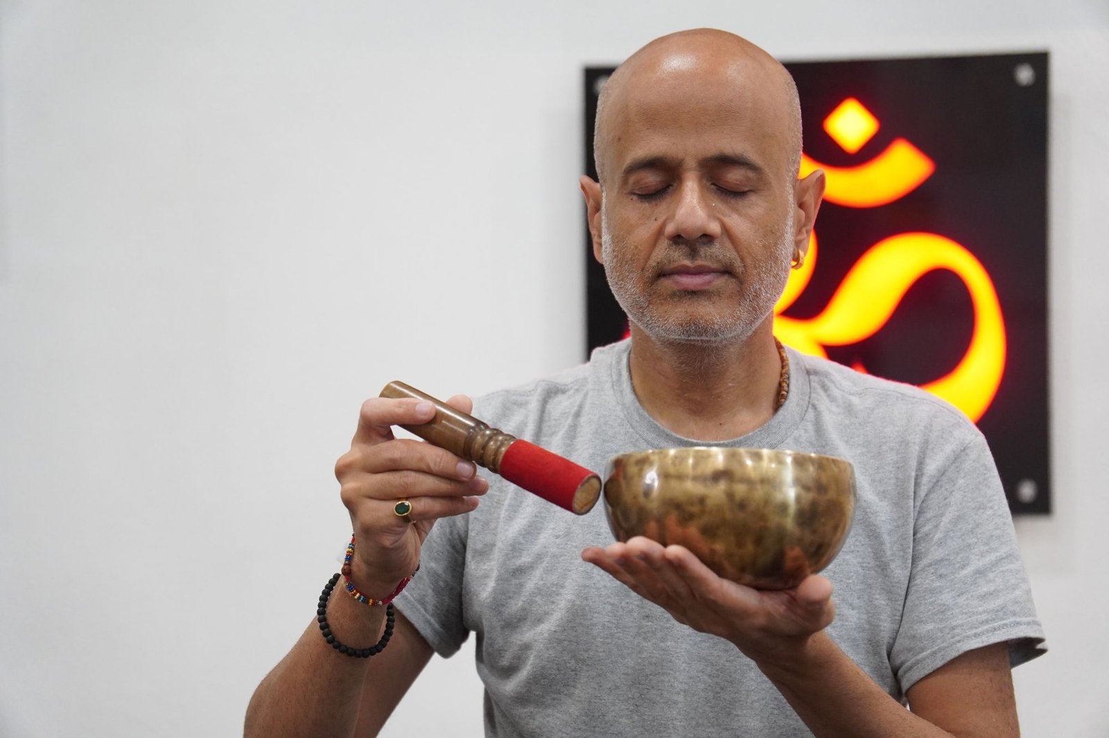 Prashant Patel playing a Himalayan singing bowl in front of a glowing Om